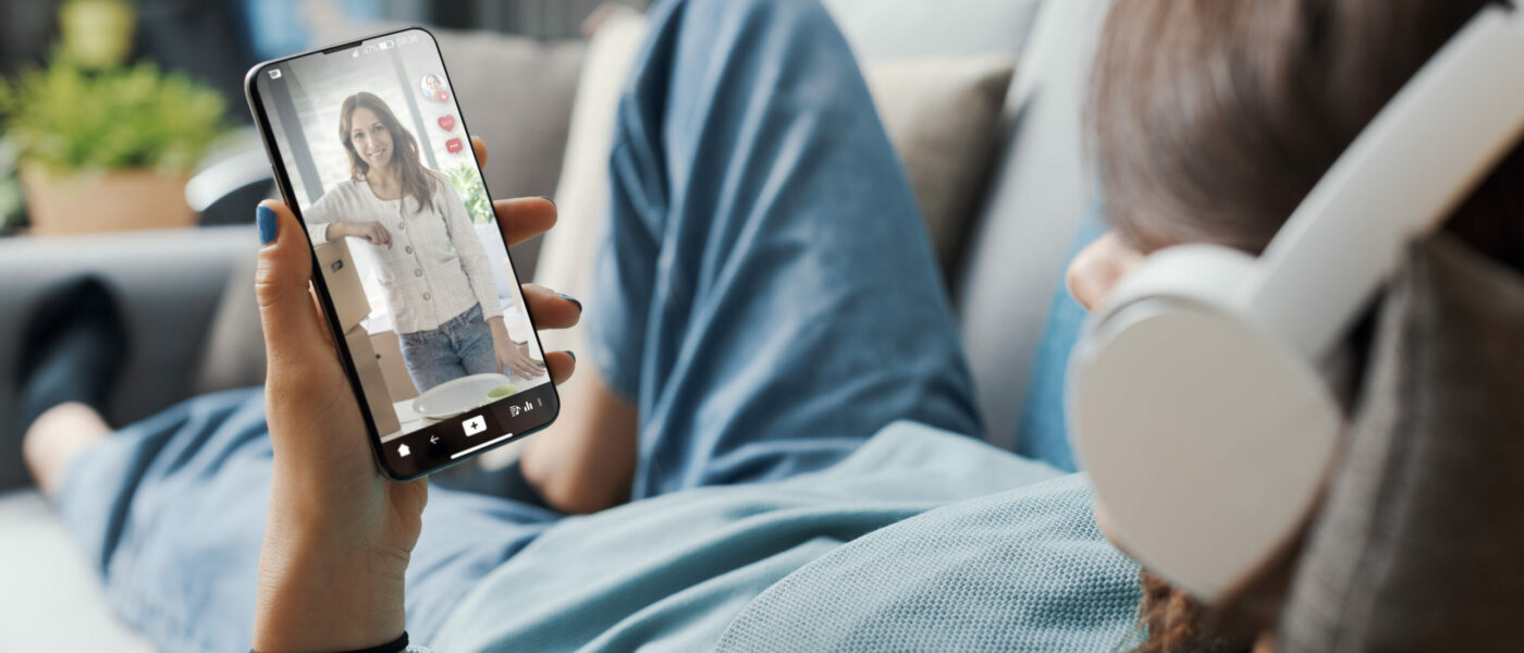 Woman lying down on the couch at home and watching social media videos on her smartphone