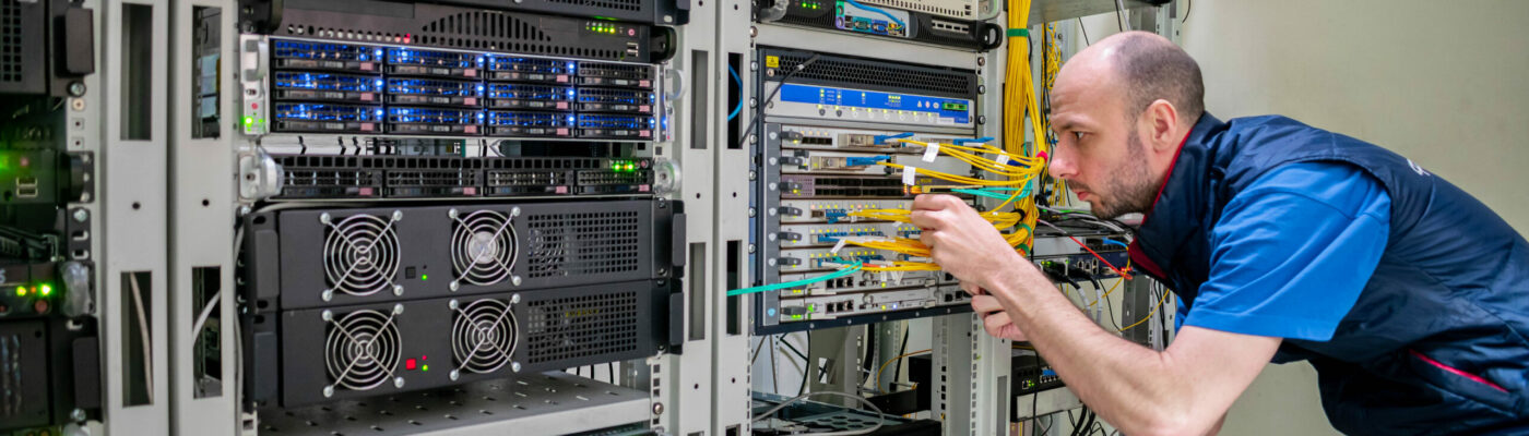 A man commutes wires in a server room. A technician works with server equipment in a data center.